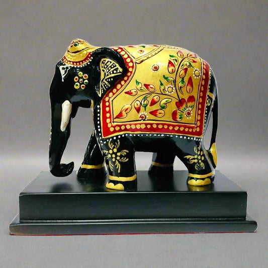 Black wooden elephant memento with gold emboss painting and multicolor floral design, standing on a wooden platform.