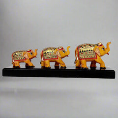Set of three hand-painted wooden elephants of varying sizes standing on a decorative wooden bridge.