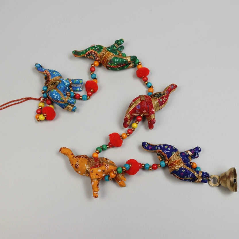 Close-up of handmade embroidered elephant hanging with decorative pompoms and a brass bell.