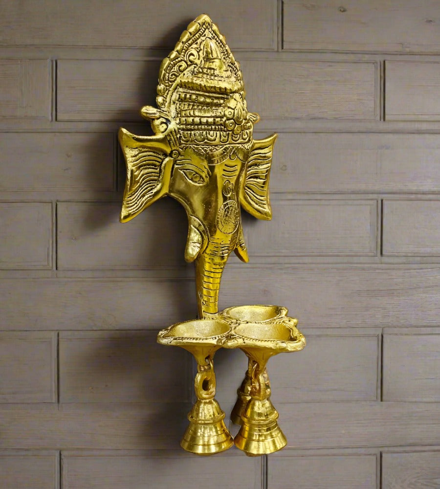 A handcrafted metal Ganesha wall hanging with a bell and diyas.
