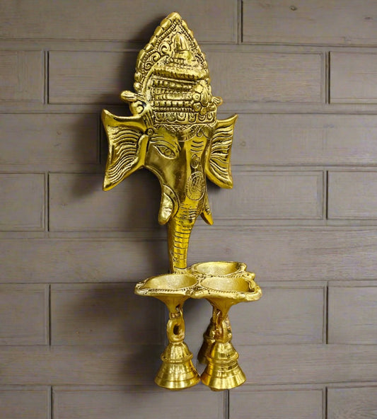 A handcrafted metal Ganesha wall hanging with a bell and diyas.