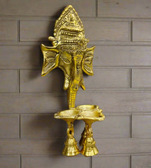 A handcrafted metal Ganesha wall hanging with a bell and diyas.