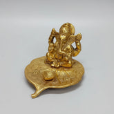 A magnificent golden oxidized metal Ganesh idol sitting on a Peepal leaf with an integrated Diya at the front.