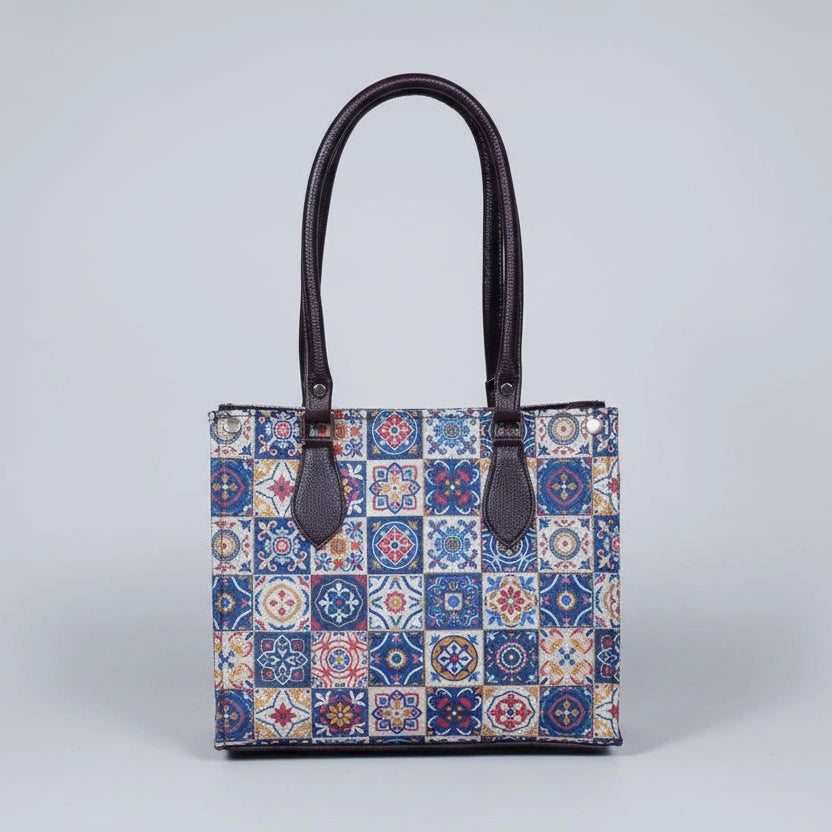 Front view of a Patola handbag featuring vibrant traditional patterns and brown synthetic PU leather handles.