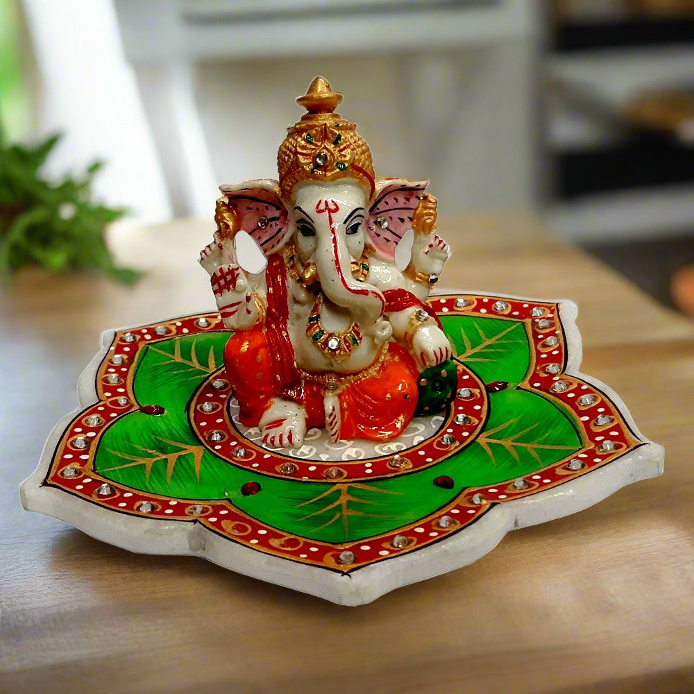 A beautiful hand-painted marble Ganesh idol seated on a lotus leaf.