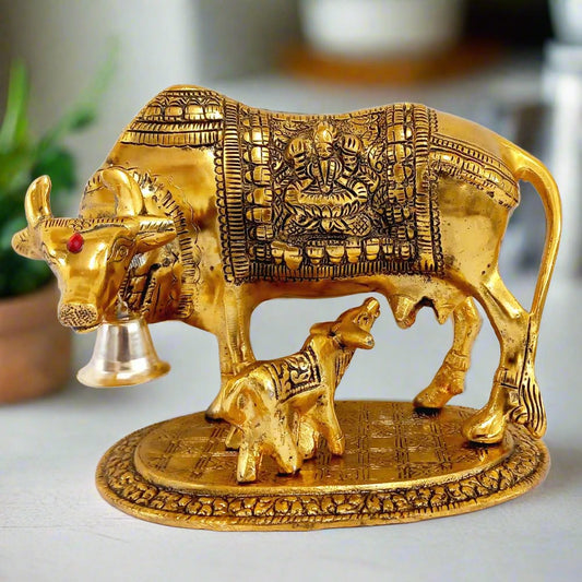 Golden oxidized metal statue of sacred Cow with Calf, featuring Lakshmi ji in front and Ganesh ji behind