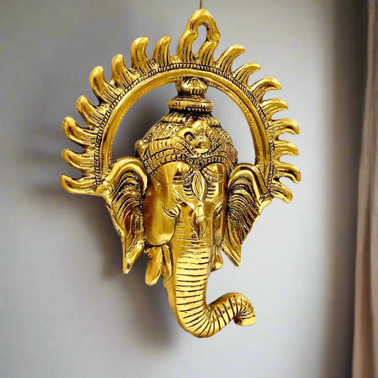 A golden metal Ganesha wall hanging with the unique shape of the sun on his face.