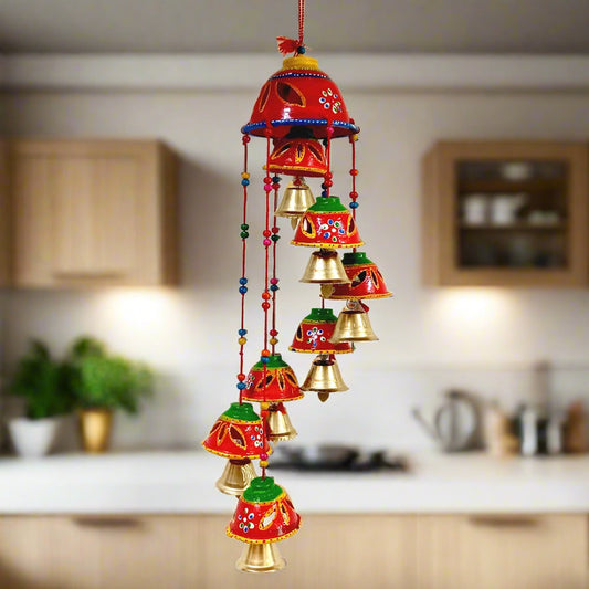 A decorative bell toran made of papier-mâché, adorned with golden bells, beads, and threads.