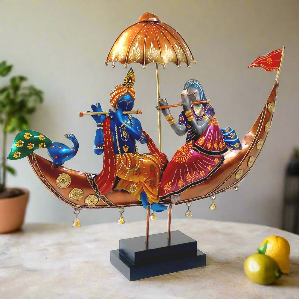 A Radha Krishna statue sitting in a boat, with a peacock, umbrella, and decorative flag.