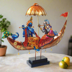 A Radha Krishna statue sitting in a boat, with a peacock, umbrella, and decorative flag.