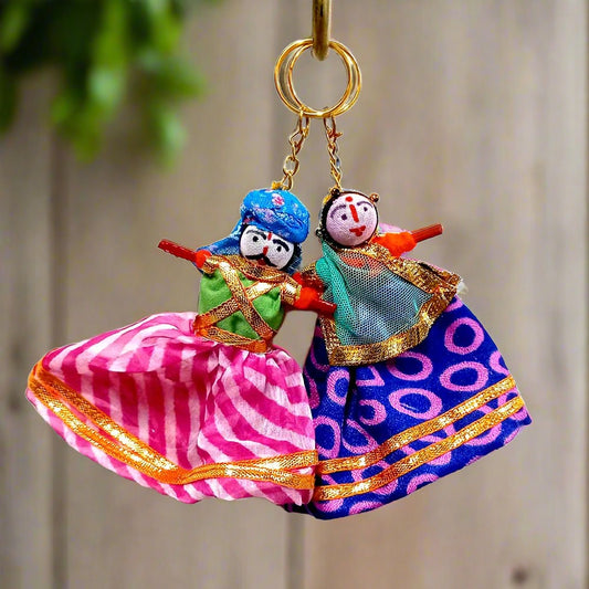 A pair of Rajasthani puppet keychains, made of fabric and wood, featuring a man and a woman.