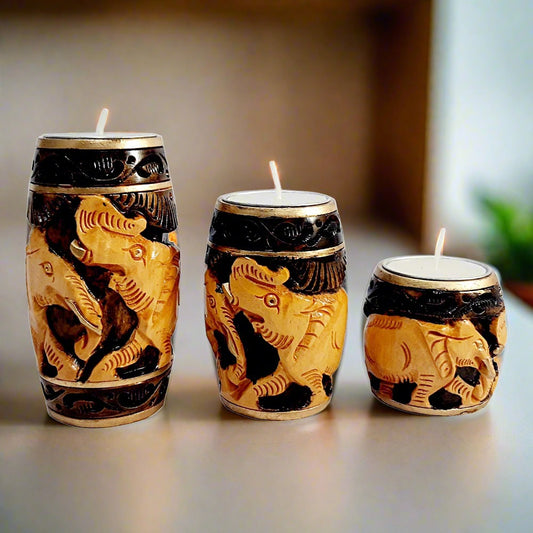 A set of 3 wooden candle holders, each with two beautifully carved elephants and a dark brown color.