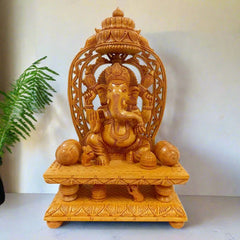 A beautiful wooden Ganesha idol seated on a throne, with a carved chhatar and splendid lattice design on the back.