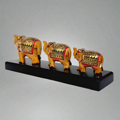 Three-piece wooden elephant set with detailed hand painting, displayed on a natural wood bridge base