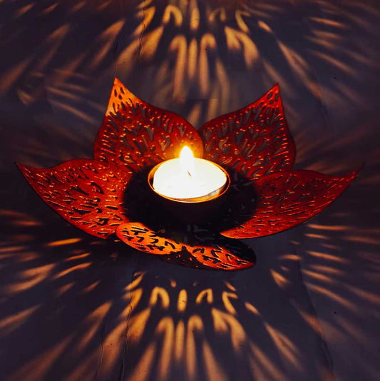 Decorative candle holder shaped like a lotus with a lit candle inside, casting shadows on a dark background.