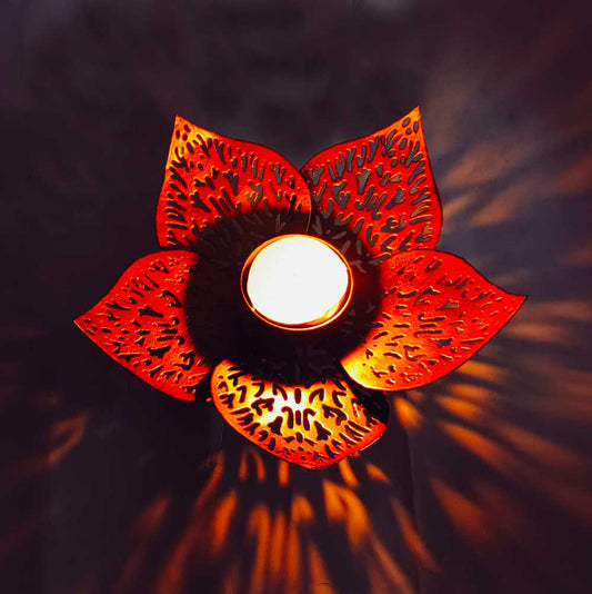Decorative red lotus-shaped tealight holder with a lit candle inside on a dark background