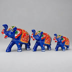 Front angled view of three blue Meenakari elephants with raised trunks and red, green and gold detailing