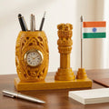 Carved wooden pen holder with a Roman numeral clock on its front, beside an Ashok Pillar and Indian flag on a wooden platform