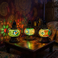 Three illuminated mosaic glass lantern lamps with colourful floral patterns on a wooden table for home decor