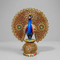 Decorative blue peacock statue with a gold-toned, stone-studded spread tail on an embellished round base