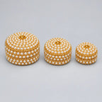 Three closed round lac kumkum boxes in graduated sizes, decorated with pearl-style bead rows, golden accents and central lid stones.