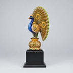 Side view of a decorative wooden peacock memento showing its blue curved neck, stone-embellished wing and green-edged feather fan.