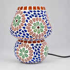 Floral mosaic glass table lamp with blue, green and reddish-brown tiles on its shade and rounded base, shown unlit.