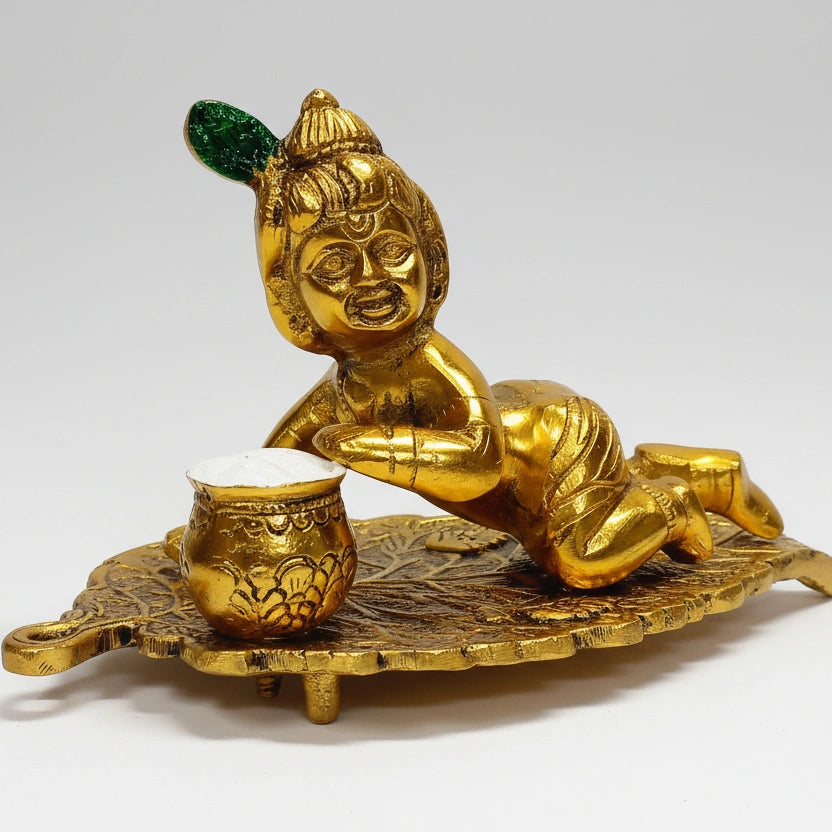 Grand golden oxidized metal idol of Laddu Gopal sitting on a leaf, eating butter.
