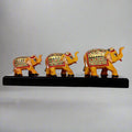 Set of three hand-painted wooden elephants of varying sizes standing on a decorative wooden bridge.