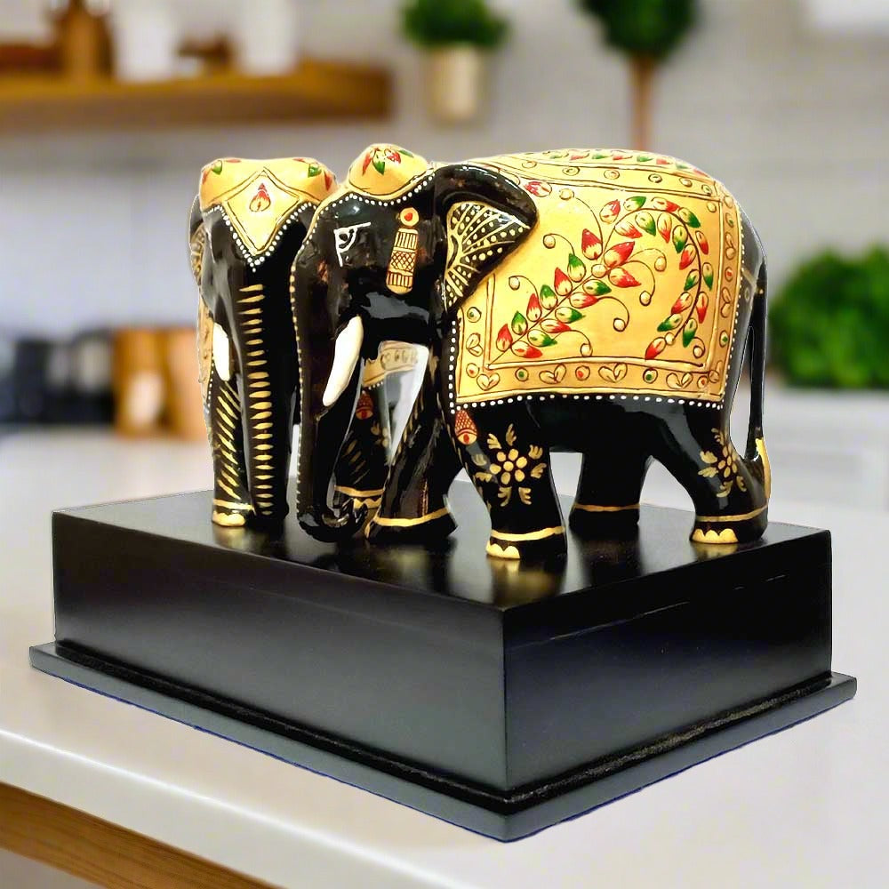An angled view of the handmade elephant statues on their black platform, highlighting the vibrant green and black color accents.