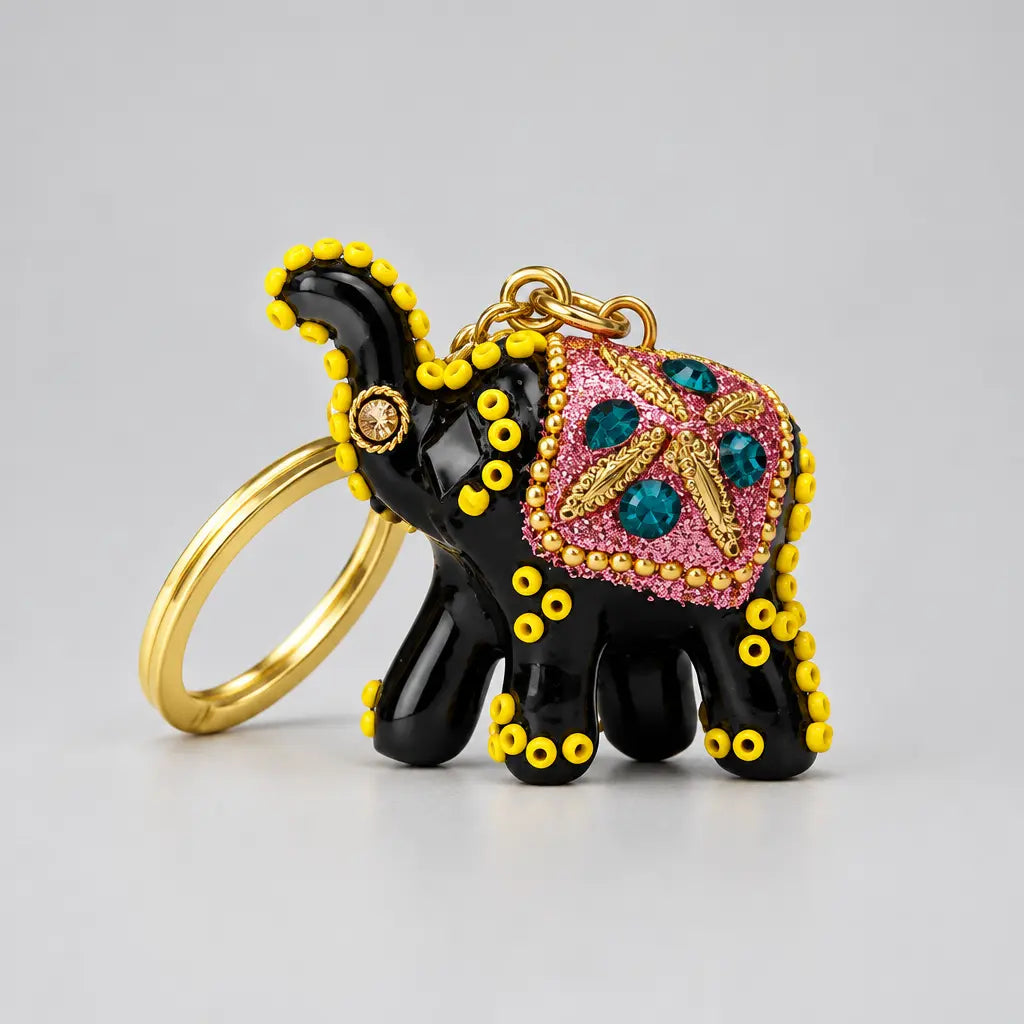 Close-up of a black lac elephant keychain with a pink glitter saddle, teal stones, gold-tone detailing and yellow accents