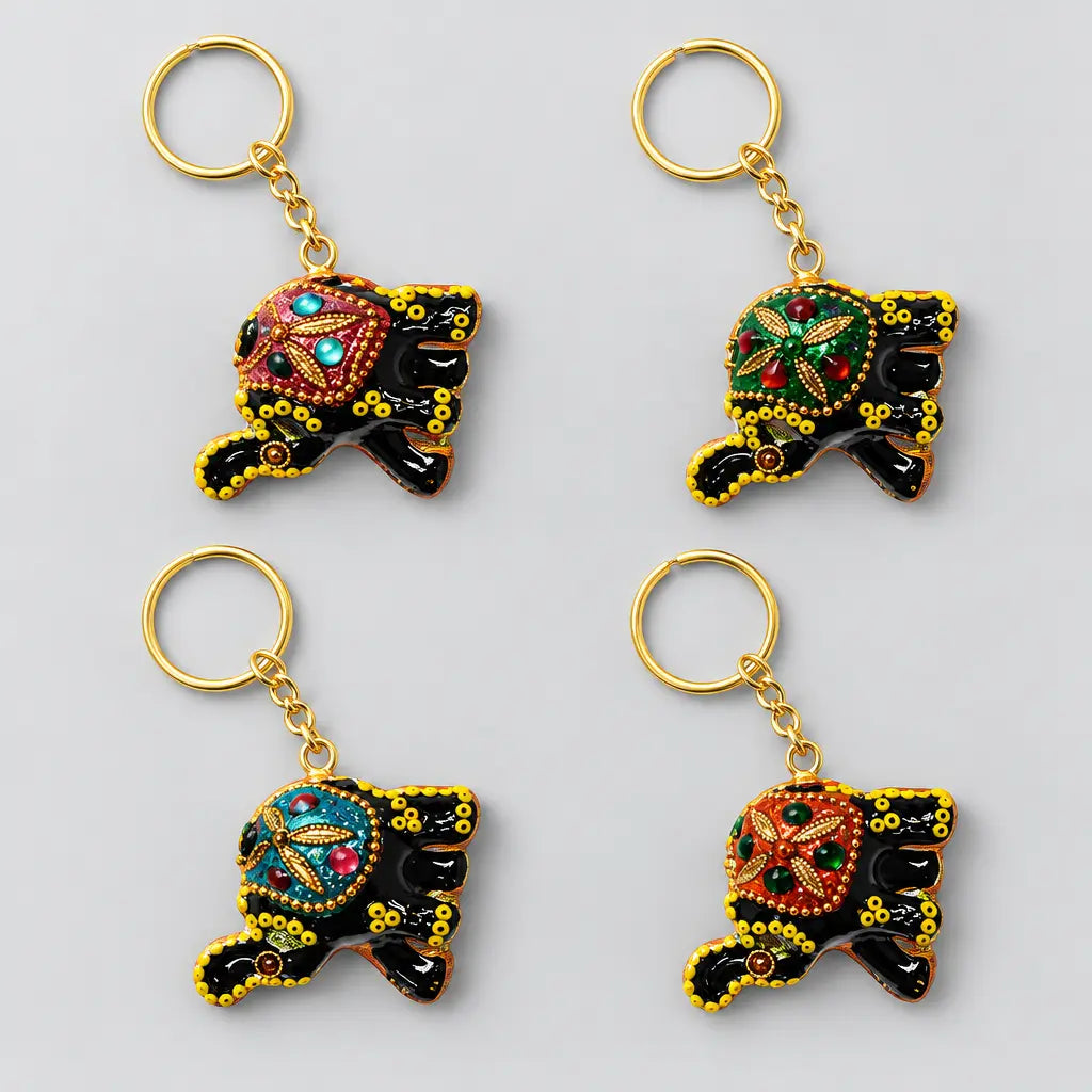 Four black lac elephant keychains in a two-by-two layout, showing pink, green, turquoise and orange embellished saddles