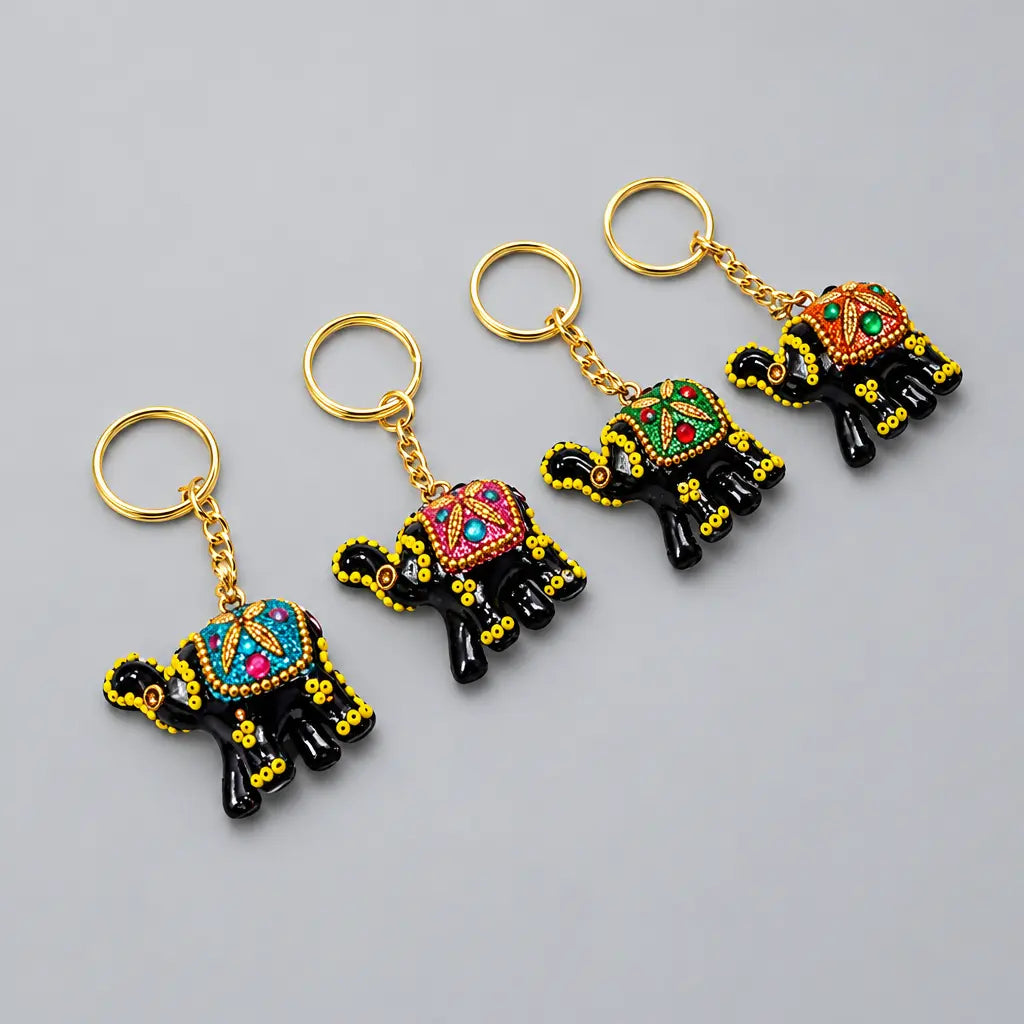 Four black lac elephant keychains with colourful decorated saddles, yellow accents and gold-tone rings