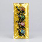 Four decorated lac elephant keychains arranged vertically inside rectangular gold-lined packaging