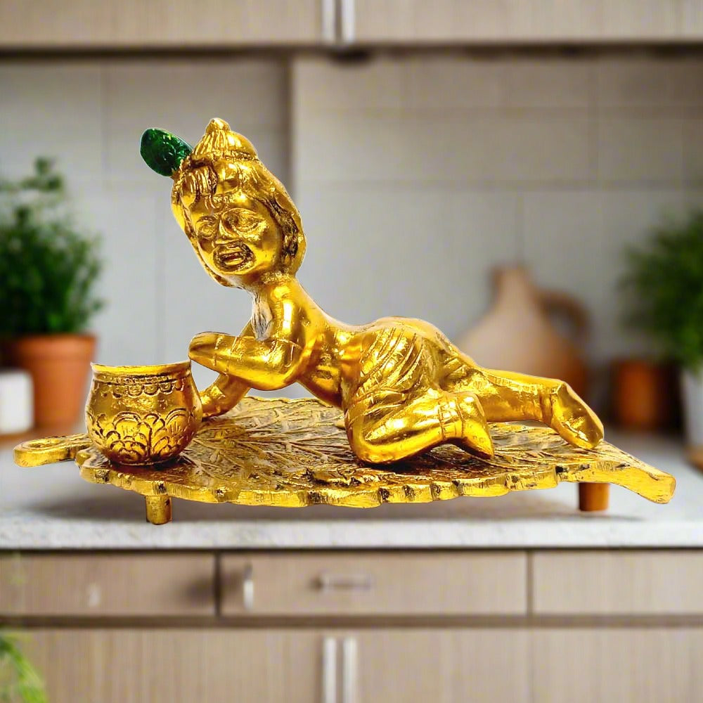 Golden oxidized Laddu Gopal idol sitting on a leaf, handcrafted in metal.