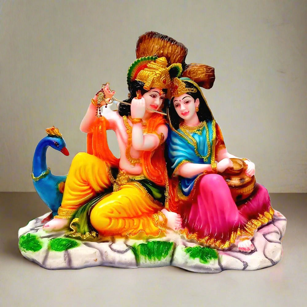 A marble dust sitting Radha Krishna idol with a peacock and a tree in the background.