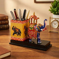 Yellow pen holder filled with pens beside a blue Meenakari Ambabari elephant on a black wooden base