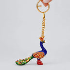 Meenakari peacock keychain hanging from a gold-tone ring, with a blue neck, green tail and floral detailing