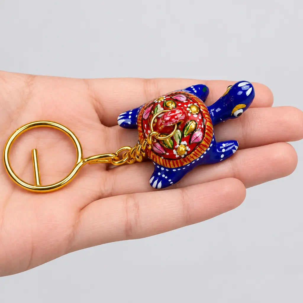 Meenakari tortoise keychain held by its gold-tone ring, showing a blue body and red shell with multicoloured floral details