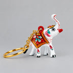 Meenakari white elephant keychain with a raised trunk, red floral saddle and gold-toned chain, facing right.
