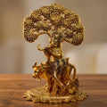 Metal Krishna idol playing the flute with a cow beneath a spreading tree