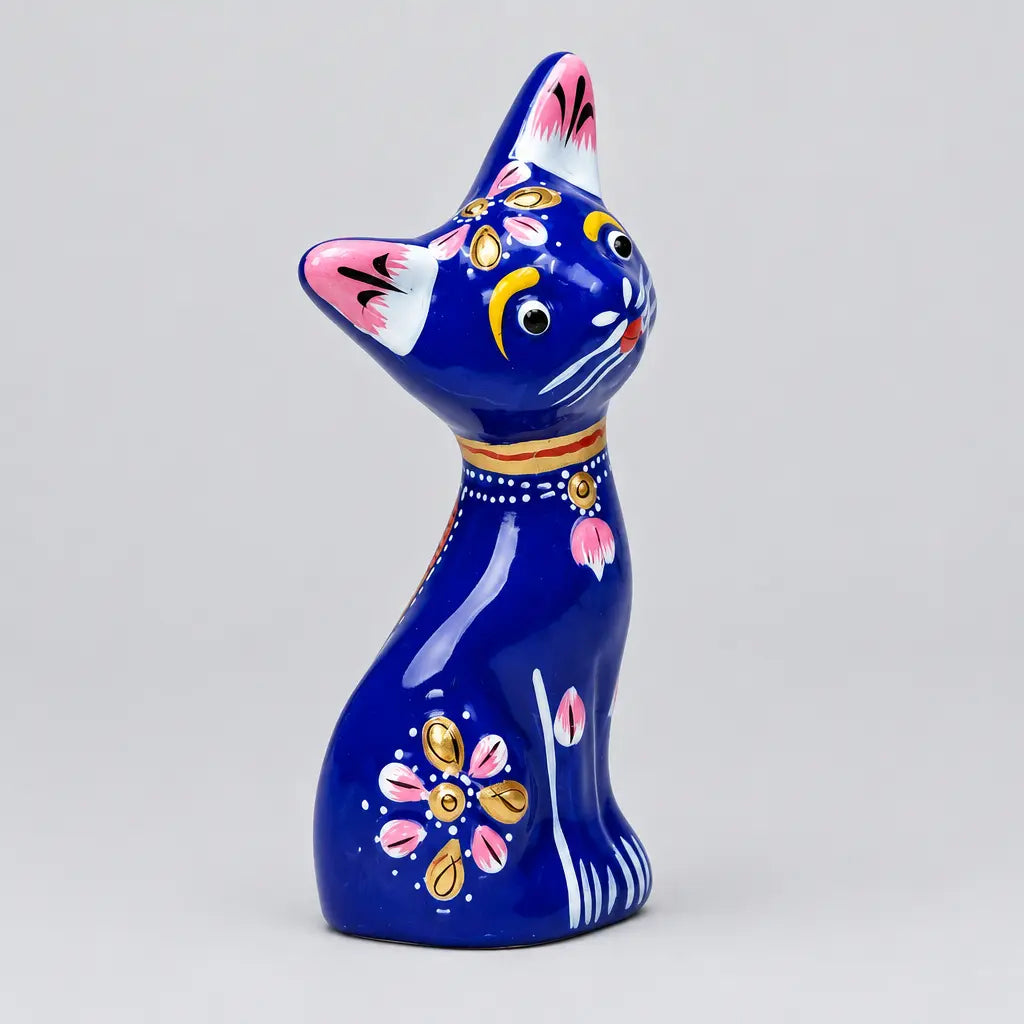 Angled view of blue metal meenakari cat statue showing pink and gold flowers and painted white paws