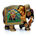 Right-facing black wooden elephant with a miniature painting of royal riders in a howdah and an attendant in a garden