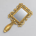 Metal hand mirror with an oxidized golden finish, rectangular glass and an ornate floral scrollwork frame and handle.