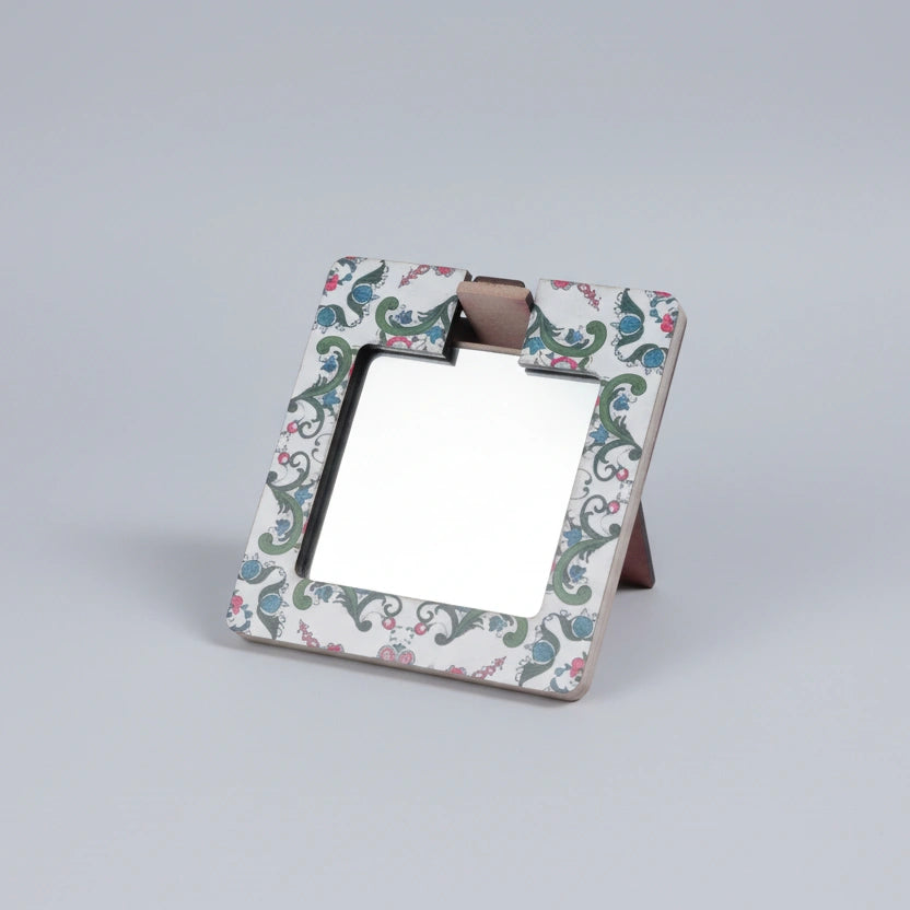 Hand holding a wooden painted pocket mirror showing the intricate printed artwork.