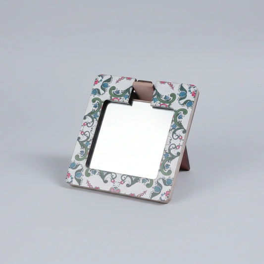 Hand holding a wooden painted pocket mirror showing the intricate printed artwork.