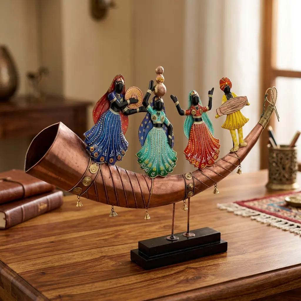 Angled view of colourful Rajasthani folk dancers and a musician on a copper toned shehnai shaped base, displayed beside books