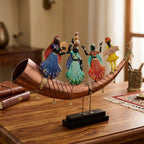 Angled view of colourful Rajasthani folk dancers and a musician on a copper toned shehnai shaped base, displayed beside books