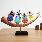 Front view of hand painted Rajasthani dancers and a dhol player on a shehnai shaped metal base with bells and a black wooden platform