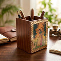 Angled view of a Sheesham wood pen holder showing its wood grain, brass border and Rajasthani gemstone painting, with pens inside.